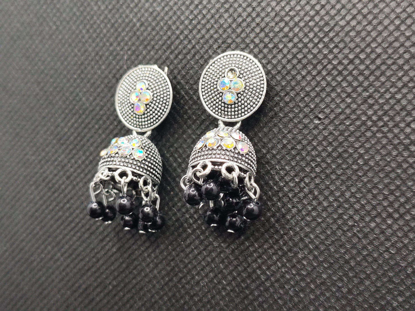 Pair of earrings with black gemstones and colorful stones on a gray textured background