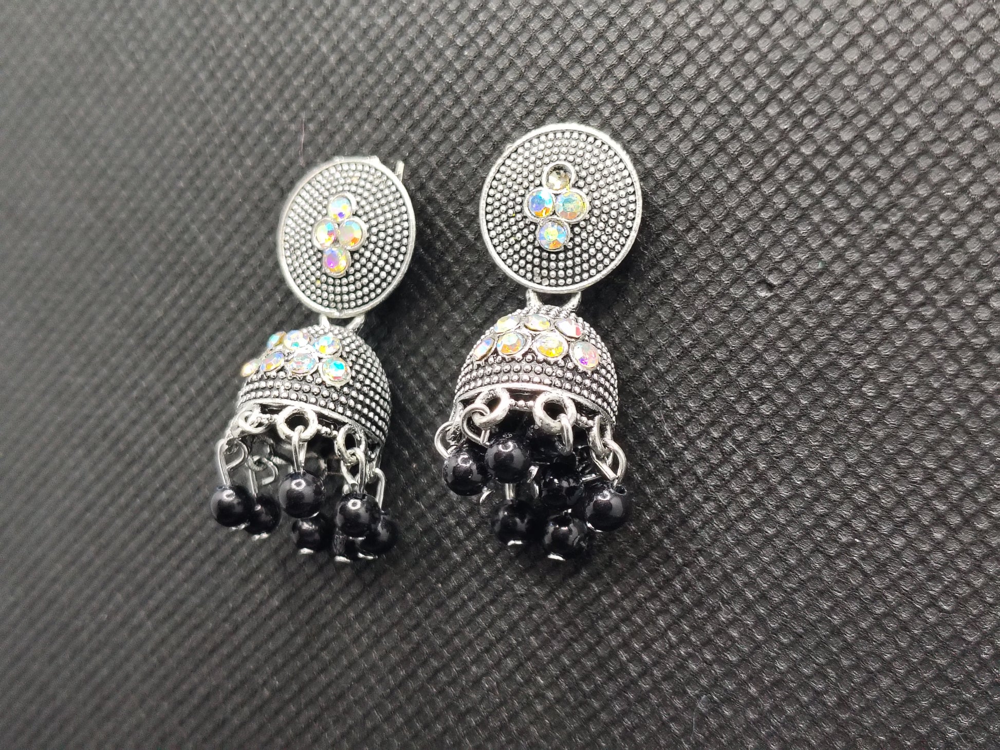 Pair of earrings with black gemstones and colorful stones on a gray textured background