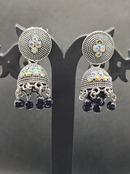 Pair of ornate earrings with gemstones on a reflective surface