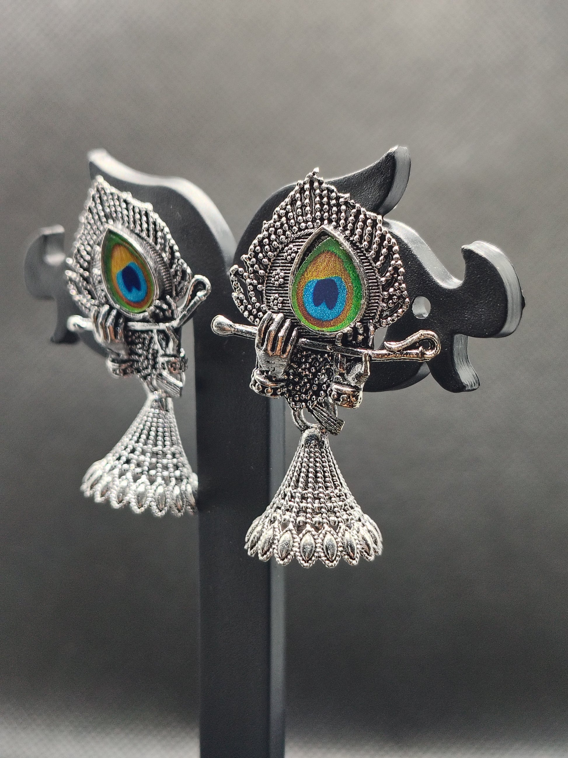 Decorative fish-shaped earrings with peacock eye design on a reflective surface.