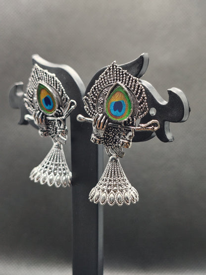 Decorative fish-shaped earrings with peacock eye design on a reflective surface.