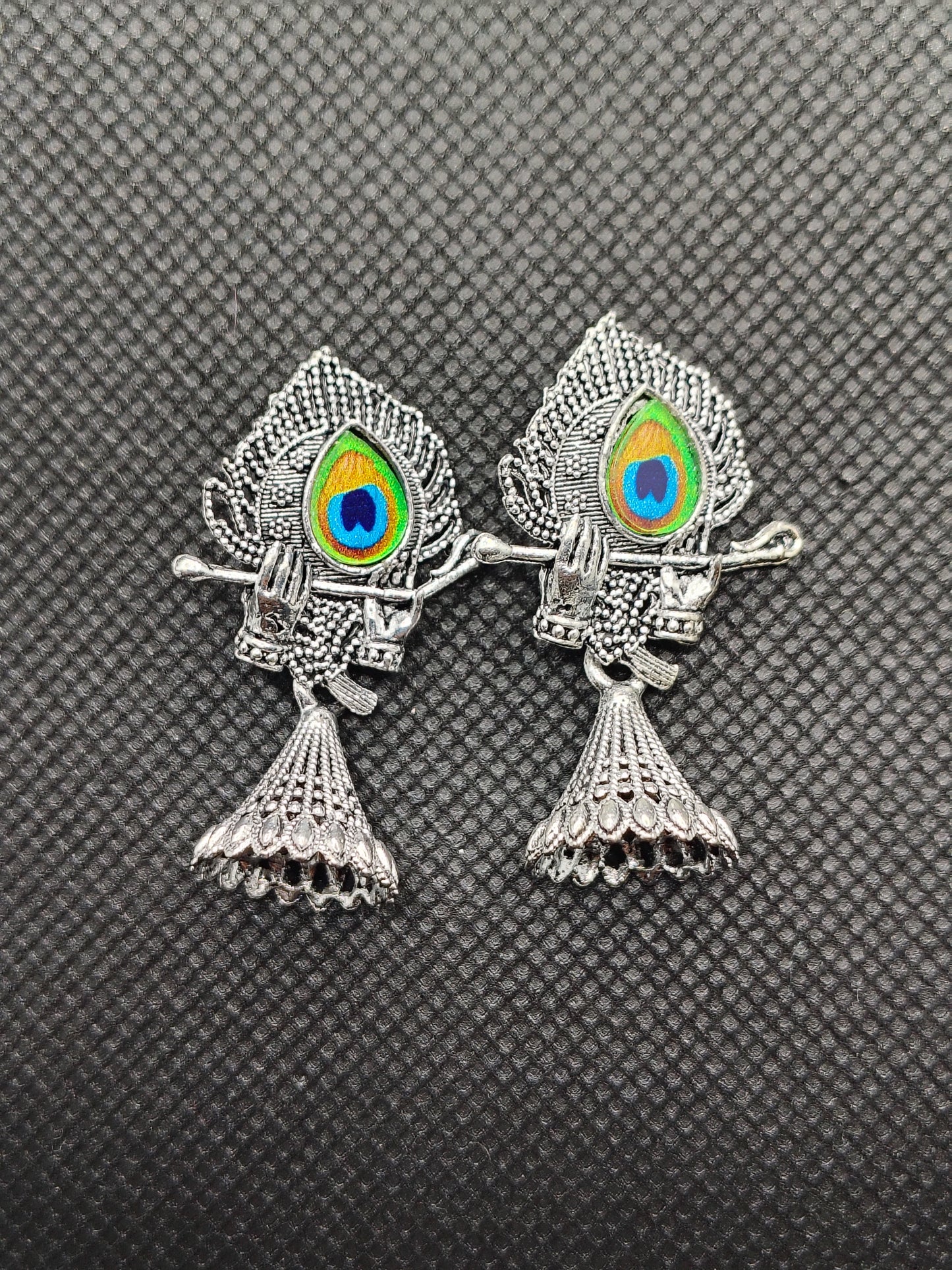 Two silver fish-shaped brooches with colorful eye designs on a textured gray background