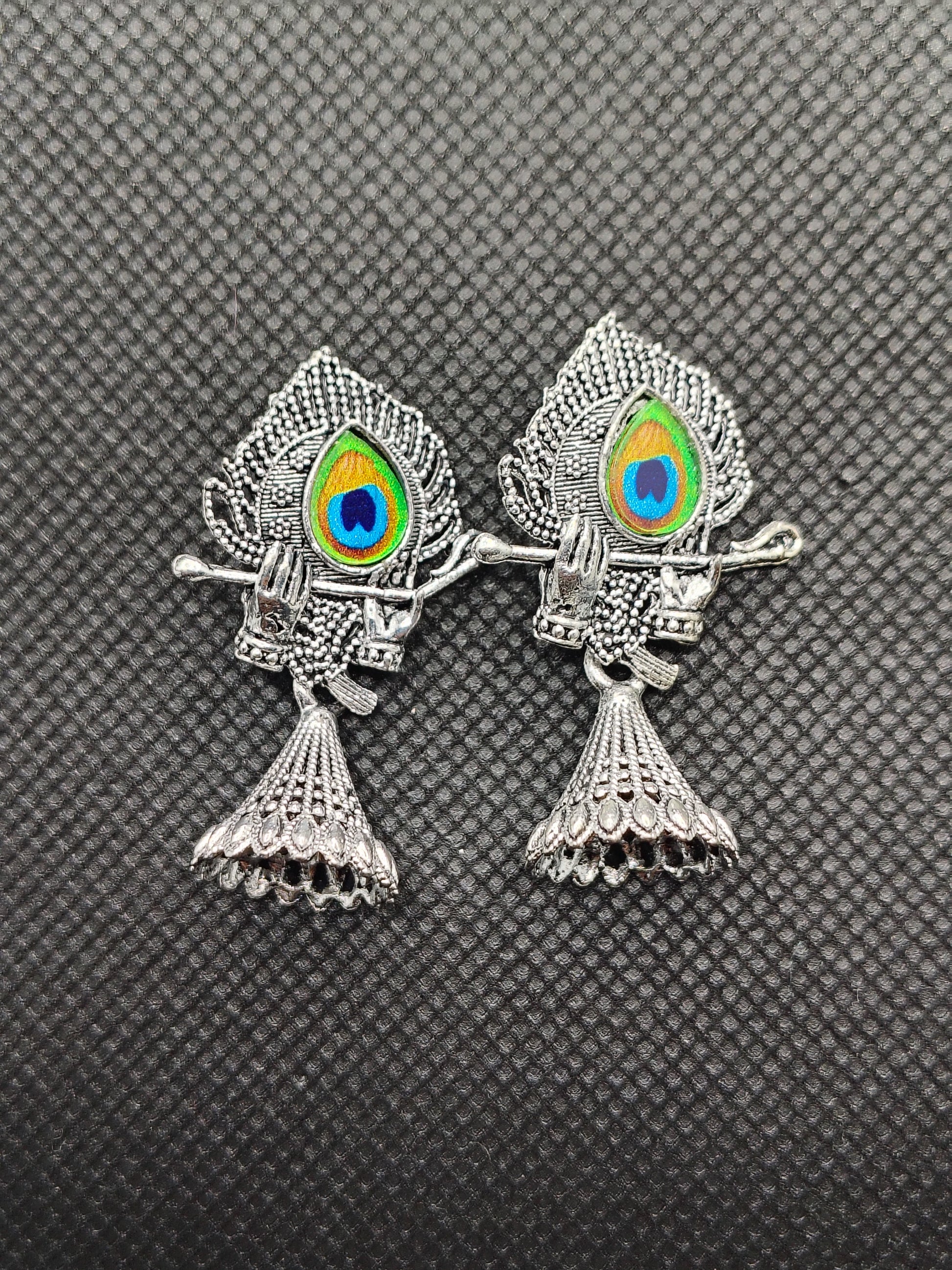 Two silver fish-shaped brooches with colorful eye designs on a textured gray background